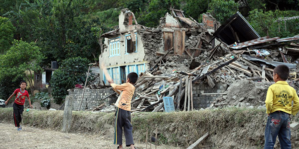 boys playing cricket outside destroyed house in nepal